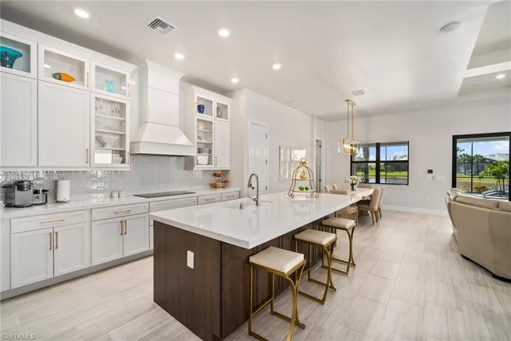 Kitchen with custom range hood, a breakfast bar area, an island with sink, black electric cooktop, and pendant lighting