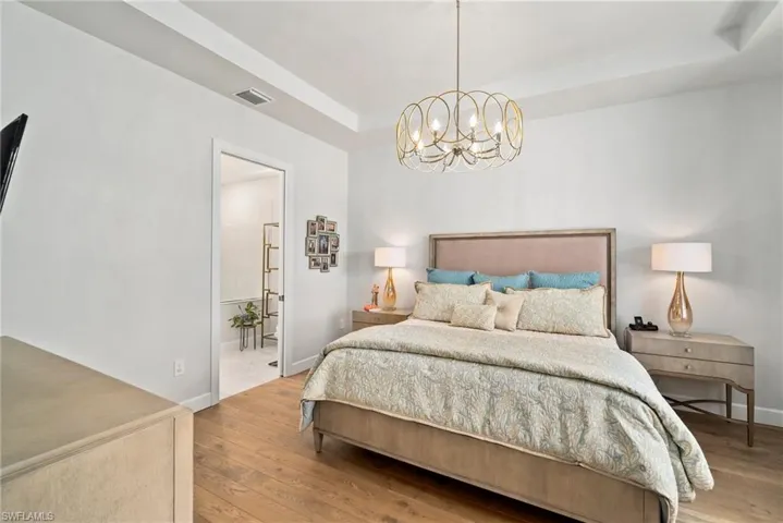 Bedroom featuring a raised ceiling, an inviting chandelier, and light hardwood / wood-style floors