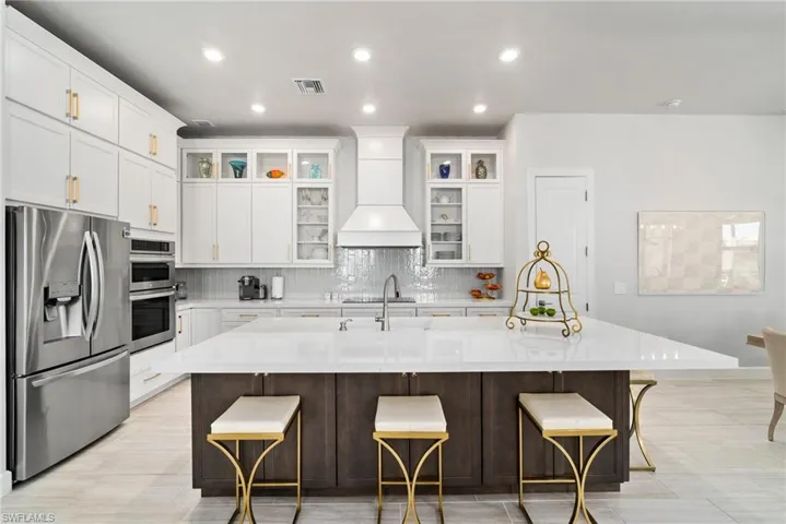Kitchen featuring appliances with stainless steel finishes, custom range hood, a kitchen bar, and a center island with sink