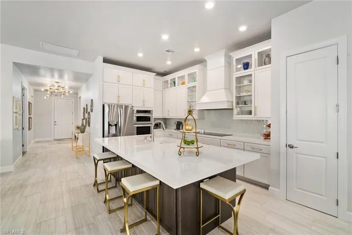 Kitchen featuring a kitchen bar, an island with sink, premium range hood, and white cabinetry