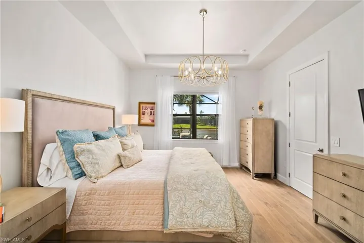 Bedroom with a raised ceiling, an inviting chandelier, and light hardwood / wood-style floors