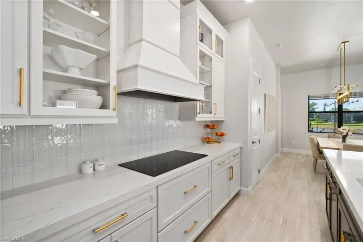 Kitchen featuring black electric stovetop, backsplash, decorative light fixtures, light stone counters, and premium range hood