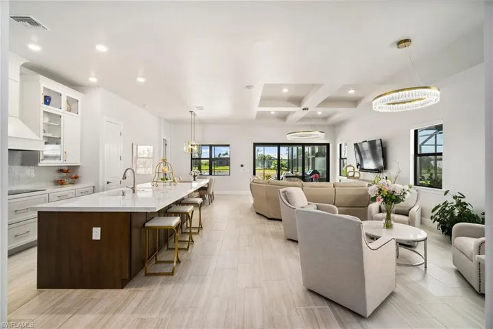 Kitchen featuring a kitchen island with sink, coffered ceiling, a kitchen bar, sink, and white cabinets