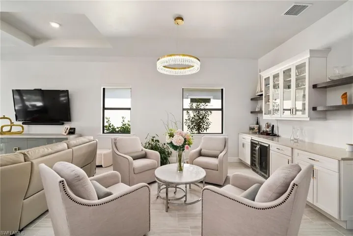 Living room featuring light wood-type flooring, beverage cooler, an inviting chandelier, a raised ceiling, and indoor bar
