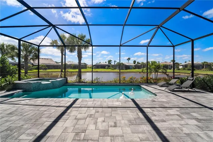 View of pool featuring a water view, a patio, glass enclosure, and an in ground hot tub