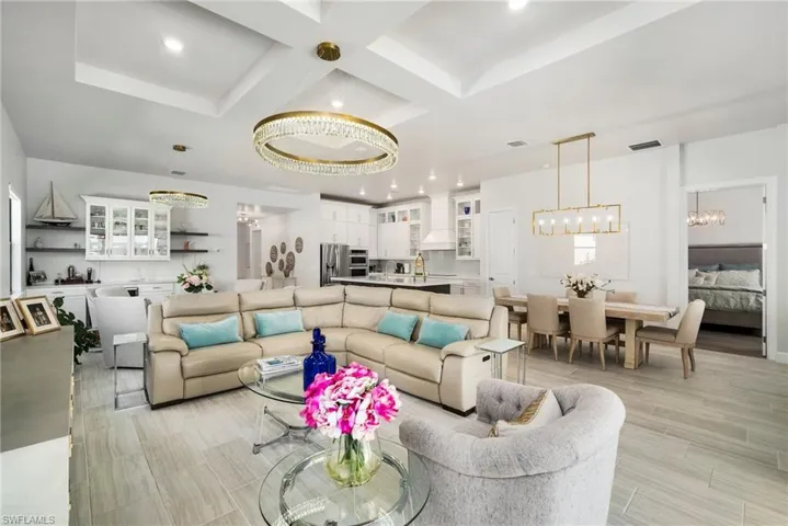 Living room featuring beamed ceiling, coffered ceiling, a notable chandelier, and light hardwood / wood-style floors