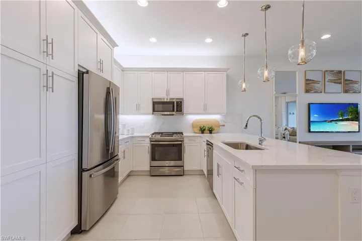 Kitchen featuring stainless steel appliances, kitchen peninsula, light stone counters, backsplash, and sink