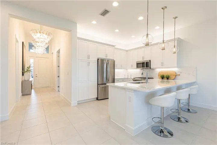 Kitchen featuring kitchen peninsula, stainless steel appliances, decorative light fixtures, backsplash, and white cabinets