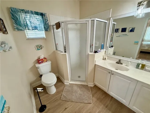 Bathroom featuring wood finished floors, toilet, a stall shower, vanity, and connected bathroom