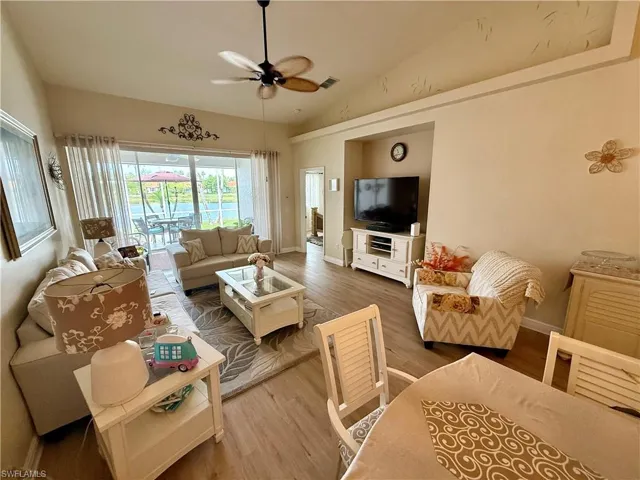 Living room with a ceiling fan, wood finished floors, lofted ceiling, and baseboards
