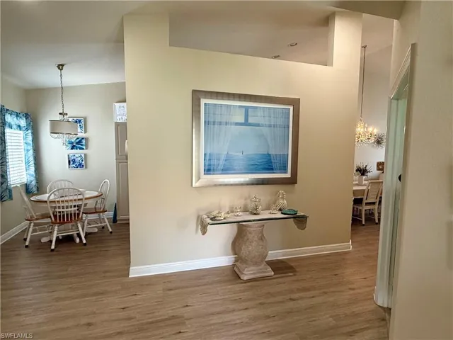 Hall with wood finished floors, baseboards, and a chandelier