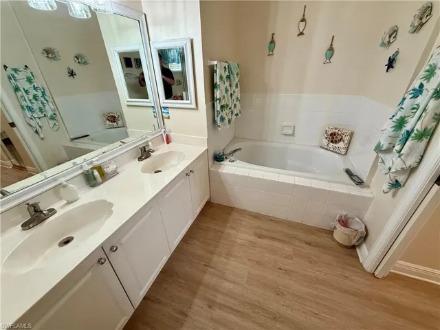 Full bathroom featuring a bath, double vanity, and wood finished floors