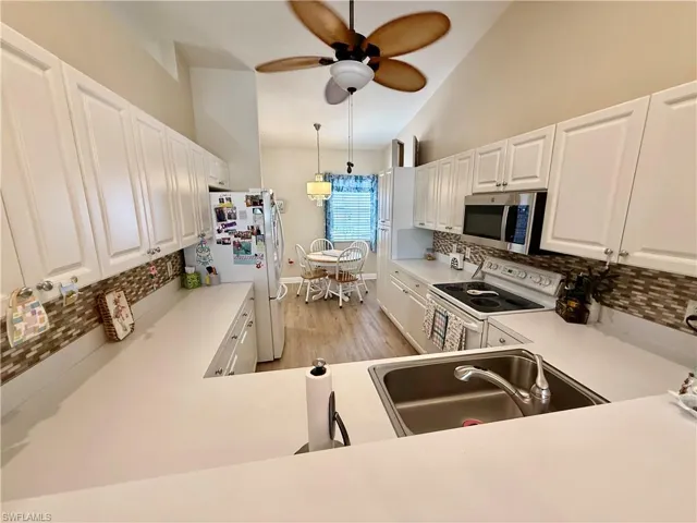 Kitchen featuring white appliances, a sink, backsplash, a ceiling fan, and vaulted ceiling