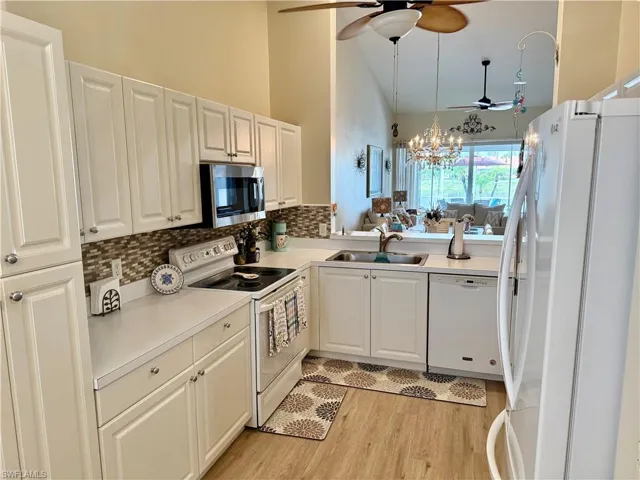 Kitchen with white appliances, a sink, ceiling fan, decorative backsplash, and light wood-style floors