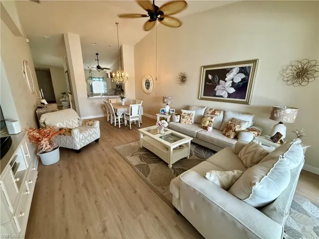Living area with a ceiling fan, wood finished floors, baseboards, and high vaulted ceiling