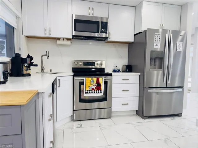 Kitchen featuring stainless steel appliances, light marble finish floors, white cabinetry, and backsplash
