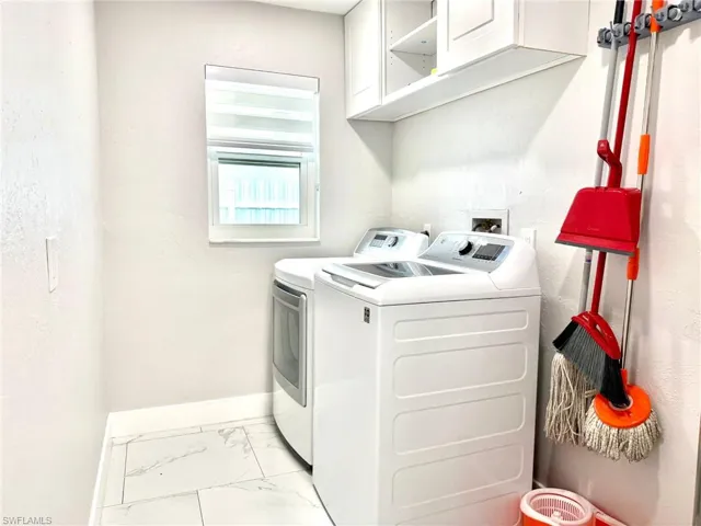 Washroom featuring light marble finish floors, cabinet space, and washer and clothes dryer
