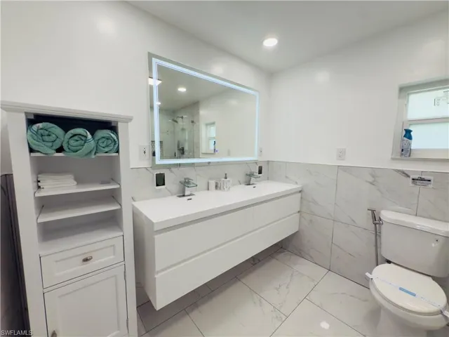 Bathroom with double vanity, light marble finish floors, a shower stall, tile walls, and recessed lighting