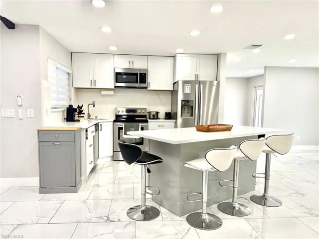 Kitchen with appliances with stainless steel finishes, gray cabinetry, a center island, a kitchen breakfast bar, and recessed lighting