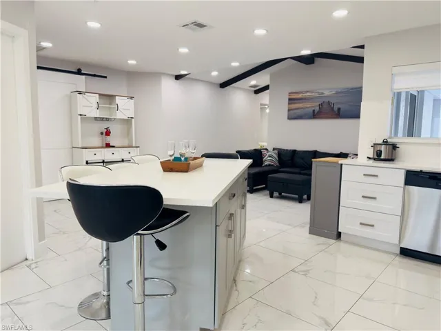 Kitchen with a barn door, a breakfast bar, light marble finish floors, light countertops, and a kitchen island