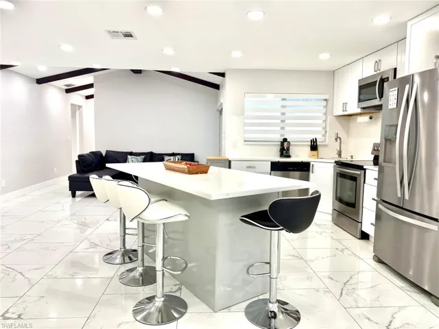 Kitchen with stainless steel appliances, white cabinets, recessed lighting, a breakfast bar area, and light marble finish floors