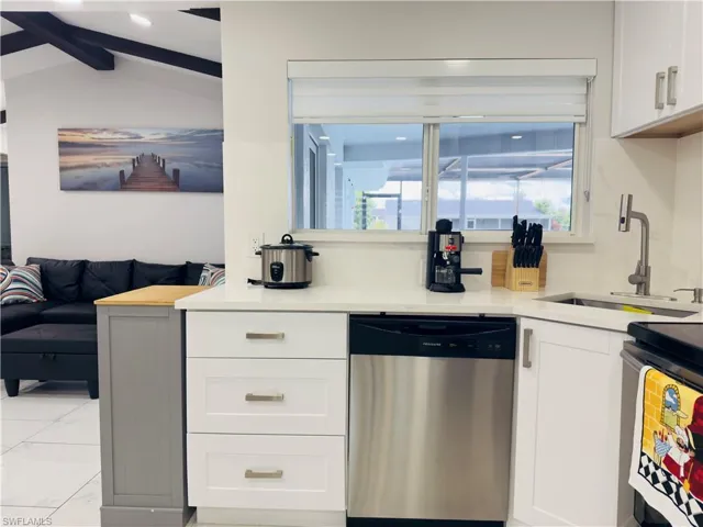 Kitchen featuring dishwasher, white cabinets, light stone countertops, and open floor plan