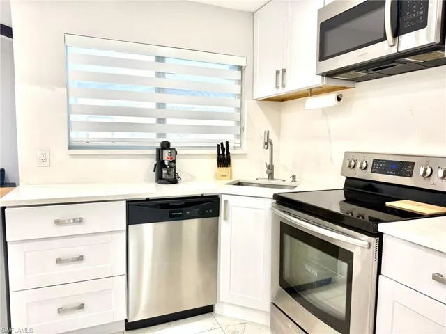 Kitchen featuring appliances with stainless steel finishes, white cabinets, light stone counters, and light marble finish flooring