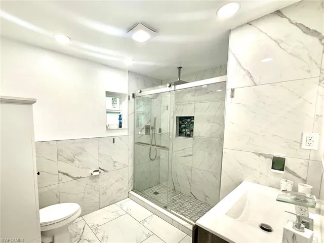 Full bath with tile walls, marble finish floors, vanity, and a marble finish shower