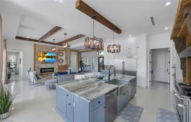 Kitchen with open floor plan, light stone countertops, premium appliances, a stone fireplace, and two tone color scheme