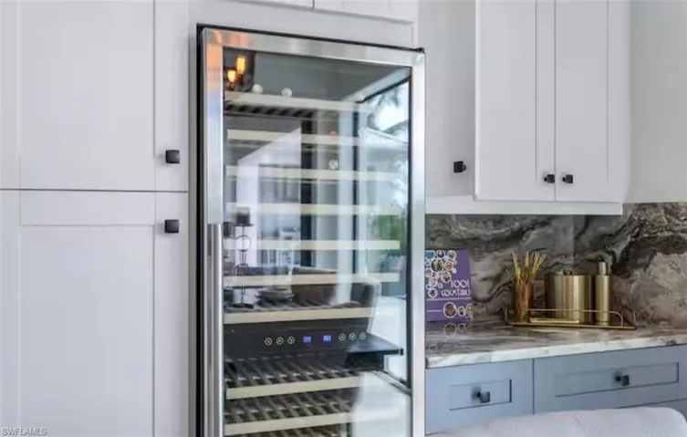 Bar area with wine cooler, decorative backsplash, light stone counters, and dual tone cabinets