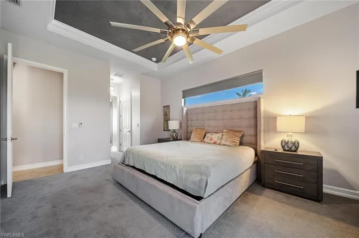 Bedroom with a tray ceiling, crown molding, a ceiling fan, baseboards, and carpet floors