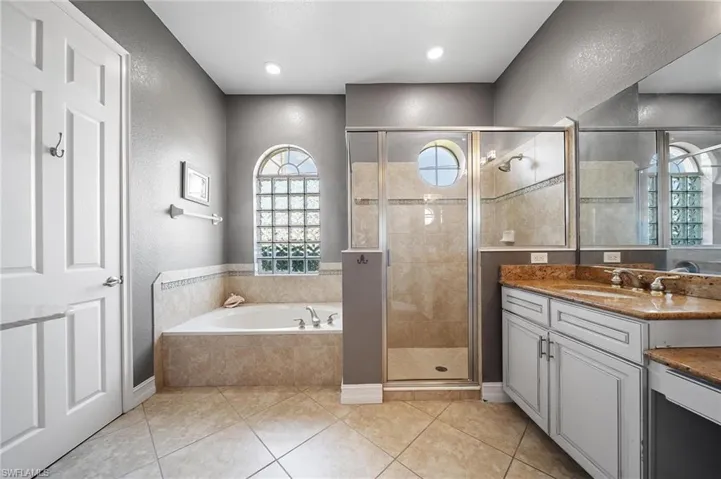 Bathroom with a textured wall, vanity, a bath, and a stall shower