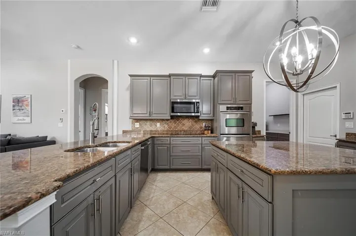 Kitchen featuring gray cabinets, arched walkways, appliances with stainless steel finishes, a sink, and visible vents