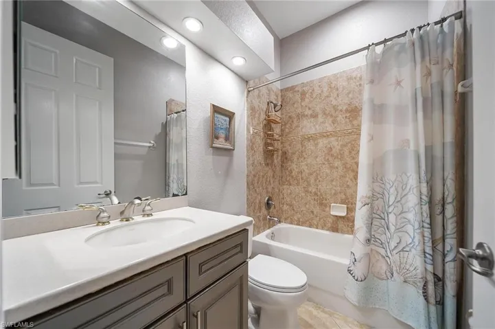 Full bath with recessed lighting, shower / bathtub combination with curtain, toilet, a textured wall, and vanity