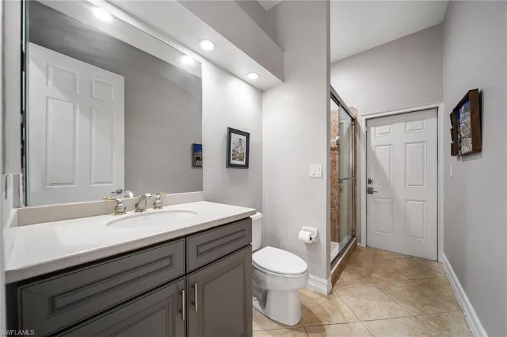 Full bath with tile patterned floors, a shower stall, toilet, vanity, and baseboards
