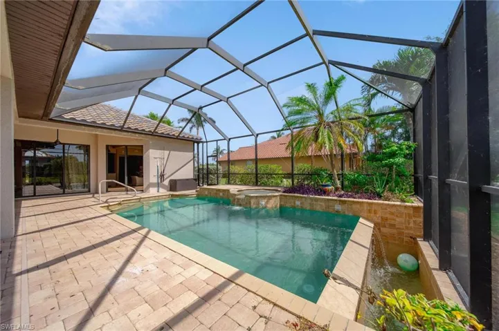 View of swimming pool featuring a patio, glass enclosure, and a pool with connected hot tub