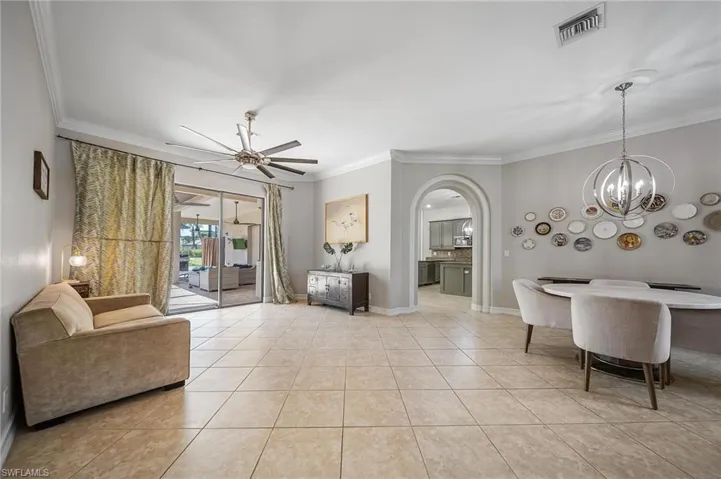 Living area with visible vents, ornamental molding, ceiling fan with notable chandelier, and arched walkways