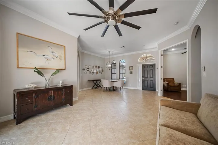 Living area featuring baseboards, arched walkways, light tile patterned flooring, ornamental molding, and a ceiling fan