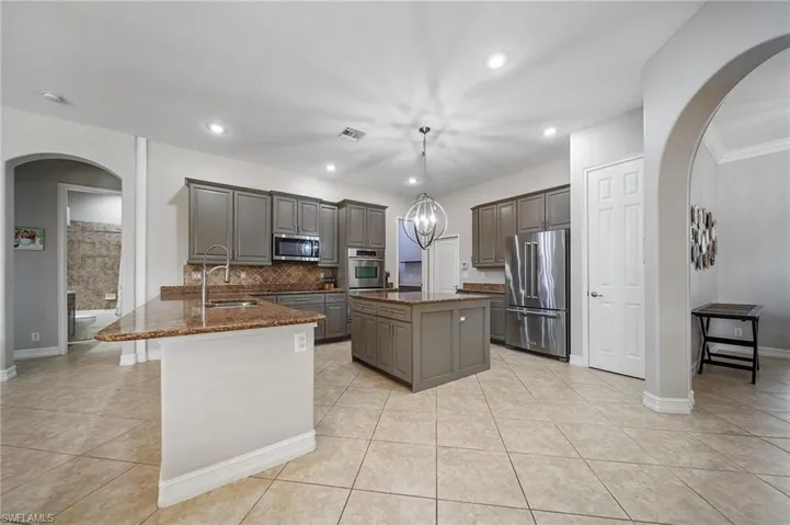 Kitchen featuring arched walkways, stainless steel appliances, a sink, a center island, and a peninsula