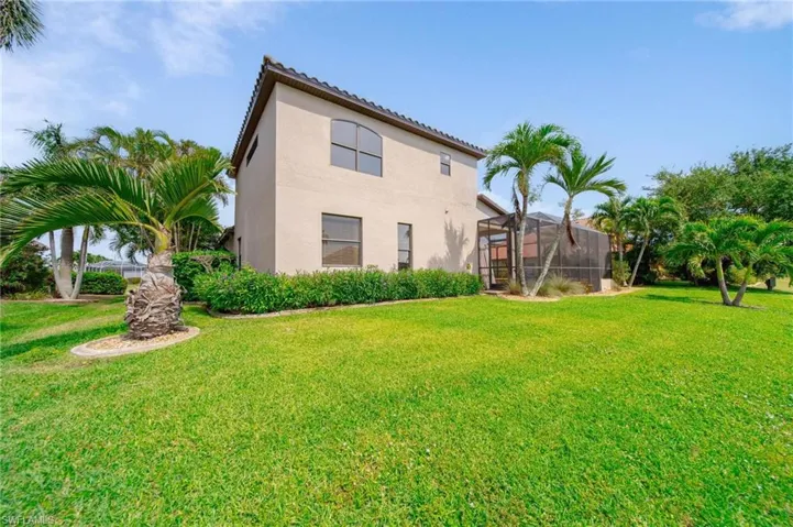 Back of house featuring stucco siding, a tiled roof, a lanai, and a yard