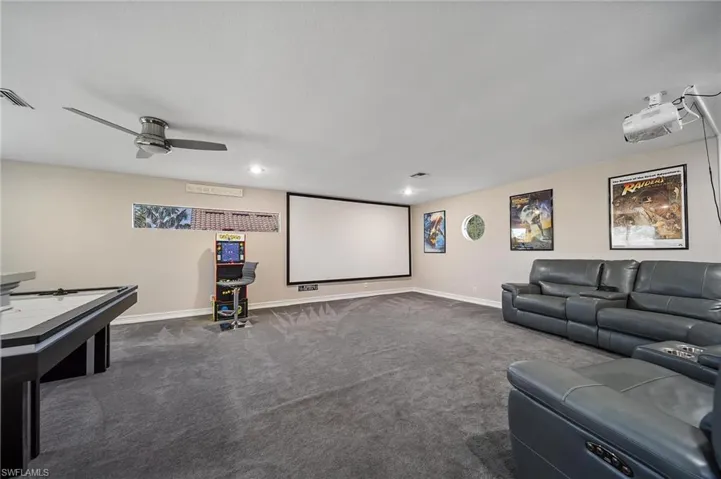Home theater with dark colored carpet, visible vents, a ceiling fan, and baseboards