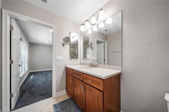 Bathroom featuring vanity, tile patterned floors, visible vents, a textured wall, and baseboards