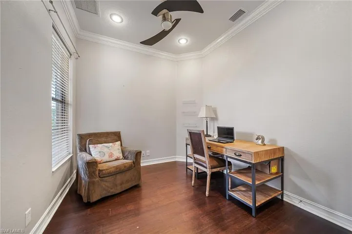 Home office with crown molding, a ceiling fan, visible vents, and wood finished floors