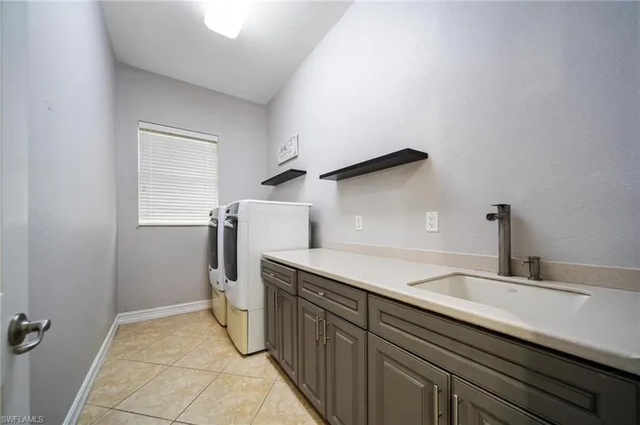 Clothes washing area with cabinet space, a sink, independent washer and dryer, light tile patterned floors, and baseboards