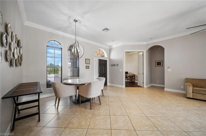 Dining room with crown molding, visible vents, arched walkways, light tile patterned flooring, and a notable chandelier