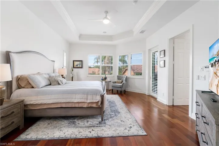 Bedroom featuring dark wood-type flooring, ornamental molding, a ceiling fan, and a raised ceiling