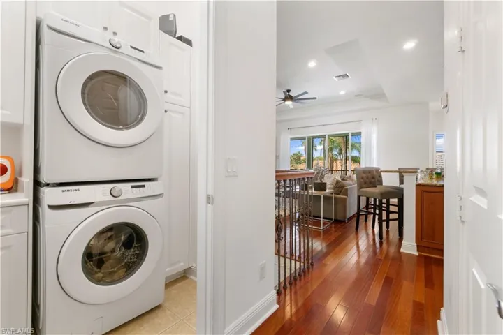 Laundry area with stacked washer / drying machine, a tray ceiling, cabinet space, dark wood-type flooring, and recessed lighting