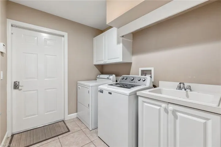 Laundry room with cabinets, sink, light tile patterned flooring, and washing machine and clothes dryer
