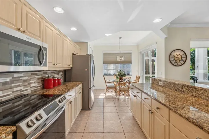 Kitchen featuring decorative backsplash, appliances with stainless steel finishes, light stone countertops, ornamental molding, and pendant lighting
