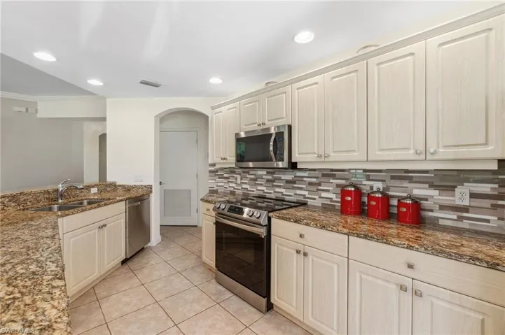Kitchen with sink, light stone countertops, tasteful backsplash, light tile patterned flooring, and stainless steel appliances